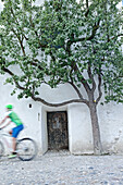 Fahrradfahrerin fährt an einer alten Tür zum Folterturm der Burg vorbei, Burghausen, Chiemgau, Bayern, Deutschland