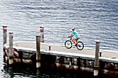 Young woman riding with her bike on a port at a lake, Lake Garda, Italy