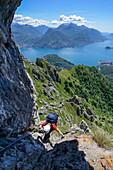 Woman climbing the Via ferrata del Centenario in front of Menaggio (right hand) at the shore of Lake Como and Grigna Settentrionale (2408 m) above it, Lombardei, Italy