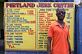 Mann vor Schild von Portland Jerk Center Grill Imbiss, Port Antonio, Portland, Jamaika, Karibik