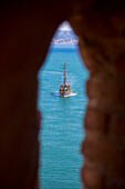 Excursion sailing boat in bay seen through opening of Kizil Kule (Red Tower), Alanya, Antalya, Turkey