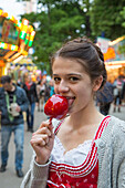 Pretty girl licks candied apple at Erlanger Bergkirchweih beer festival and fair, Erlangen, Franconia, Bavaria, Germany