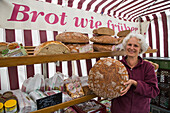 Woman presents large loaf of bread at Lebe Gesund market stand at the Farmer's Market on Marktplatz market square, Erlangen, Franconia, Bavaria, Germany