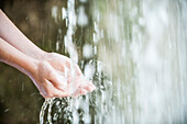 Child holding hands under waterfall, cropped
