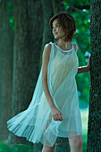 Young woman in dress walking amongst trees, looking over shoulder