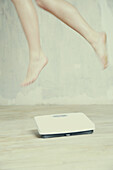 Woman's legs in mid-air above bathroom scale