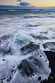 Eisblöcke bei Sonneuntergang an schwarzem Lavastrand, die vom Gletschersee Jökulsarlon  am Vatnajökull-Gletscher angespült werden, Breidamerkursandur zwischen dem Skaftafell-Nationalpark und Höfn, Ostisland, Island, Europa