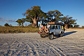 Familie sitzt auf einem Geländwagen im Sonnenuntergang, Tutume, Nxai-Pan-Nationalpark, Botswana