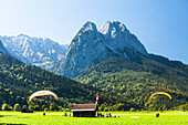 Gleitschirmflieger landen auf einer Wiese unter dem Waxenstein, Garmisch-Partenkirchen, Bayern, Deutschland