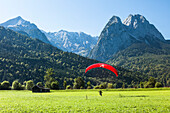 Gleitschirmflieger landet auf einer Wiese, im Hintergrund Alpspitz, Jubiläumsgrat und Waxenstein, Garmisch-Partenkirchen, Bayern, Deutschland