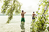 two young men going for a swim in Lake Starnberg near a birch tree, Berg, Upper Bavaria, Germany