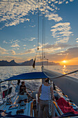 A young man sitting at the steering wheel, steering a sailing yacht at sunset, Mallorca, Balearic Islands, Spain, Europe