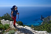 Eine junge Frau wandert entlang der gebirgigen Küste, Felsnadel bei Pedra Longa im Hintergrund, Selvaggio Blu, Sardinien, Italien, Europa