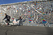 Frau fährt Fahrrad vorbei an der Berliner Mauer, East Side Gallery, Friedrichshain, Berlin, Deutschland