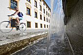 Junge Fahrradfahrerin fährt an einem Brunnen vorbei, Kempten, Bayern, Deutschland