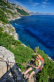 Woman rapelling over rockface, Mediterranean in background, Selvaggio Blu, National Park of the Bay of Orosei and Gennargentu, Sardinia, Italy
