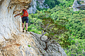 Woman hiking Selvaggio Blu over rock ledge, Selvaggio Blu, National Park of the Bay of Orosei and Gennargentu, Sardinia, Italy