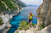 Woman hiking Selvaggio Blu over rock ledge with view to bay, Selvaggio Blu, National Park of the Bay of Orosei and Gennargentu, Sardinia, Italy