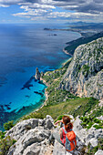 Frau beim Wandern sitzt an Punta Giradili und blickt auf Golfo di Orosei mit Felsnadel Pedra Longa, Selvaggio Blu, Nationalpark Golfo di Orosei e del Gennargentu, Sardinien, Italien