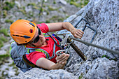 Woman anchoring carabiners at fixed rope route, fixed rope route Pidinger Klettersteig, Hochstaufen, Chiemgau Alps, Chiemgau, Upper Bavaria, Bavaria, Germany