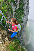 Woman ascending on ladder to Steineberg, fog in background, Steineberg, Nagelfluh range, Allgaeu Alps, Allgaeu, Svabia, Bavaria, Germany