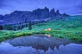 Frau sitzt in erleuchtetem Zelt, Sellastock spiegelt sich in Bergsee, Sellagruppe, UNESCO Weltnaturerbe Dolomiten, Dolomiten, Trentino, Italien