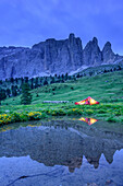 Frau sitzt in erleuchtetem Zelt, Sellastock spiegelt sich in Bergsee, Sellagruppe, UNESCO Weltnaturerbe Dolomiten, Dolomiten, Trentino, Italien