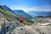 Woman hiking ascending towards Hinterseejoch, lake Vordersee in background, Lechtal Alps, Tyrol, Austria