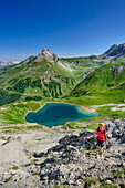 Woman hiking ascending towards Kridlonscharte, lake Hintersee, Alplespleisspitze and Feuerspitze in background, Lechtal Alps, Tyrol, Austria