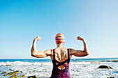 Older Caucasian woman flexing her muscles on beach, Los Angeles, California, USA