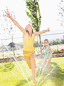 Caucasian girls playing in sprinkler in backyard, Lehi, Utah, USA