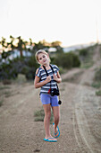 Caucasian girl carrying camera on rural dirt road, Santa Fe, New Mexico, USA