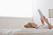 Caucasian woman laying in bed reading paperwork, Saint Louis, MO, USA