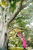 Acrobatic Caucasian girl hanging on fabric under tree, C1