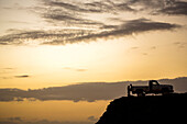 Silhouette of people sitting on pickup truck on cliff at sunset, C1