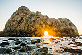 Sun shining through rock formation to ocean waves, Big Sur, California, United States, Big Sur, California, United States