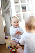 A 10 months baby girl, smiling in front of a mirror