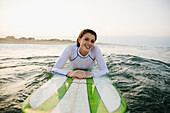 Smiling Caucasian teenage girl leaning on surfboard in ocean
