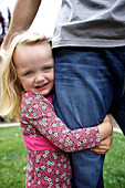Caucasian girl hugging father's leg