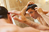 Hispanic man inspecting hair in bathroom mirror