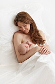 Nude Caucasian woman breast-feeding newborn baby