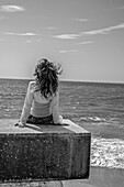 Young Girl Sitting on Stone Slab Looking out to Sea, Rear View