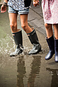 Two Young Girls Walking Through Puddle in Rubber Boots