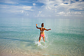 A young woman runs into shallow turquoise water while on vacation in Cayo Coco, Cuba.