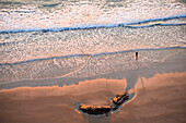 Waves greet a fisherman on the beach on the coast of Cornwall, the United Kingdom while the sunsets in front of him.