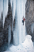 'Ice climber Sam Elias delicately moves his way up a large ice pillar during a blizzard in a seldom frozen area known as the ''Ice Palace'' in Rifle Colorado. He is wearing a red jacket and stands out on the ice formation and a heavy amount of snow is cle