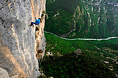 A horizontal image of a women in a blue jacket rappelling into the Verdon Gorge in France. The Verdon Gorge is considered Europe's Grand Canyon and has shear rock walls of limestone as high as 1,000 feet.