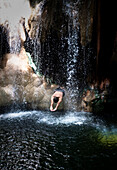 A man dives through a waterfall fed by hot springs and lands in the cool river flowing below.  This swimming hole is called Finca Paraiso and sits 40 minutes from the Guatemalan town of Rio Dulce.