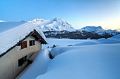 Enchanted atmosphere during the blue hour at Alp Spluga, with some scattered huts covered in snow, Graubunden, Swiss Alps, Switzerland, Europe