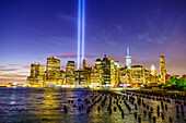 Lower Manhattan skyscrapers including One World Trade Center from across the East River at night, with light beams from the Tribute in Light 9/11 Memorial, New York City, New York, United States of America, North America